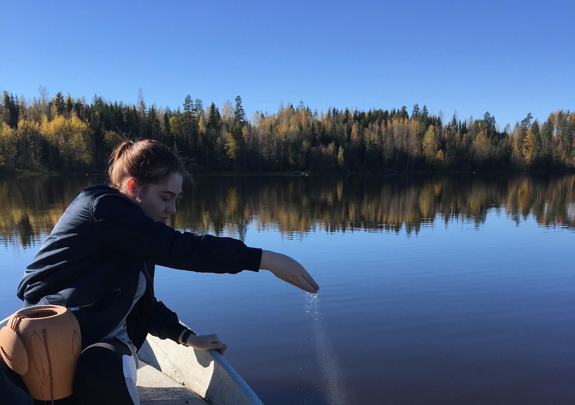 A girl scattering ashes somewhere in USA on a serene lake during autumn