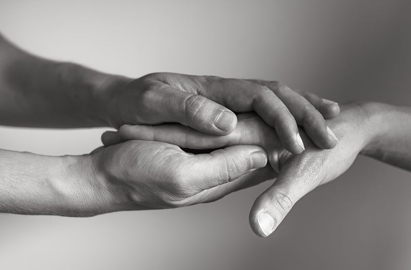 Two hands clasping another person's hand in between, forming a symbol of support.